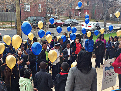 Students hold blue and gold balloons outside of their school.