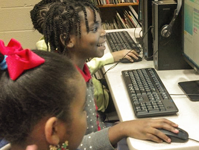 Elementary school students smile while seated at computers