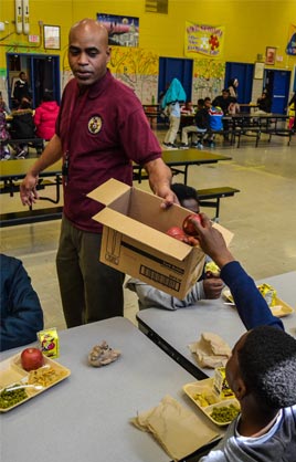 DCPS male staff member collecting apples from students in a card board box