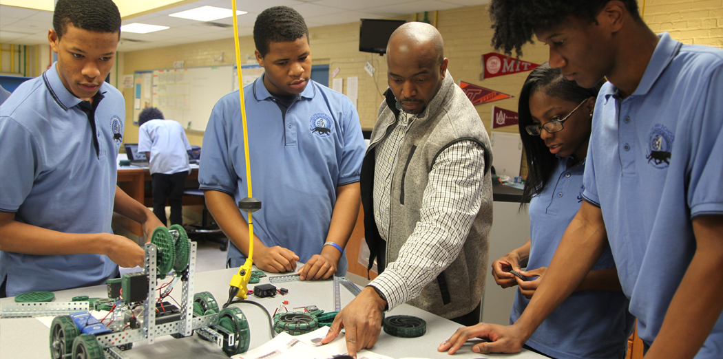 High school students surrounding a teacher instructing them on robotics