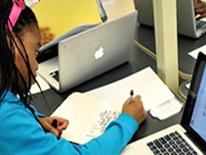 Student using both paper and computer for classwork Photo of young girl doing work on paper and on computer